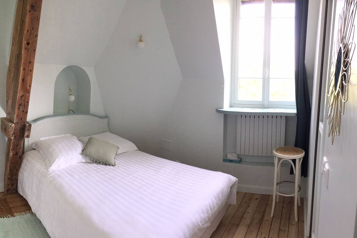 Een slaapkamer met een bed, een raam, een radiator en een houten stoel.