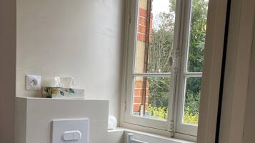 A small, clean bathroom with a toilet, a towel rack, a radiator, and a window with a view of greenery.