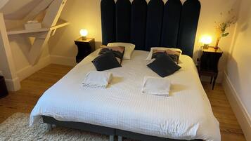 Een net opgemaakt bed met witte lakens en twee gevouwen handdoeken, een donker hoofdbord en twee bedlampjes.
