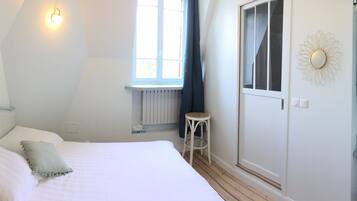 Un dormitorio con cama, ventana, radiador, taburete, toallero y espejo.