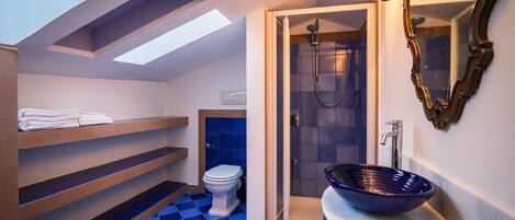 A modern bathroom with a skylight, a walk-in shower, a blue checkered floor, and a large vessel sink.