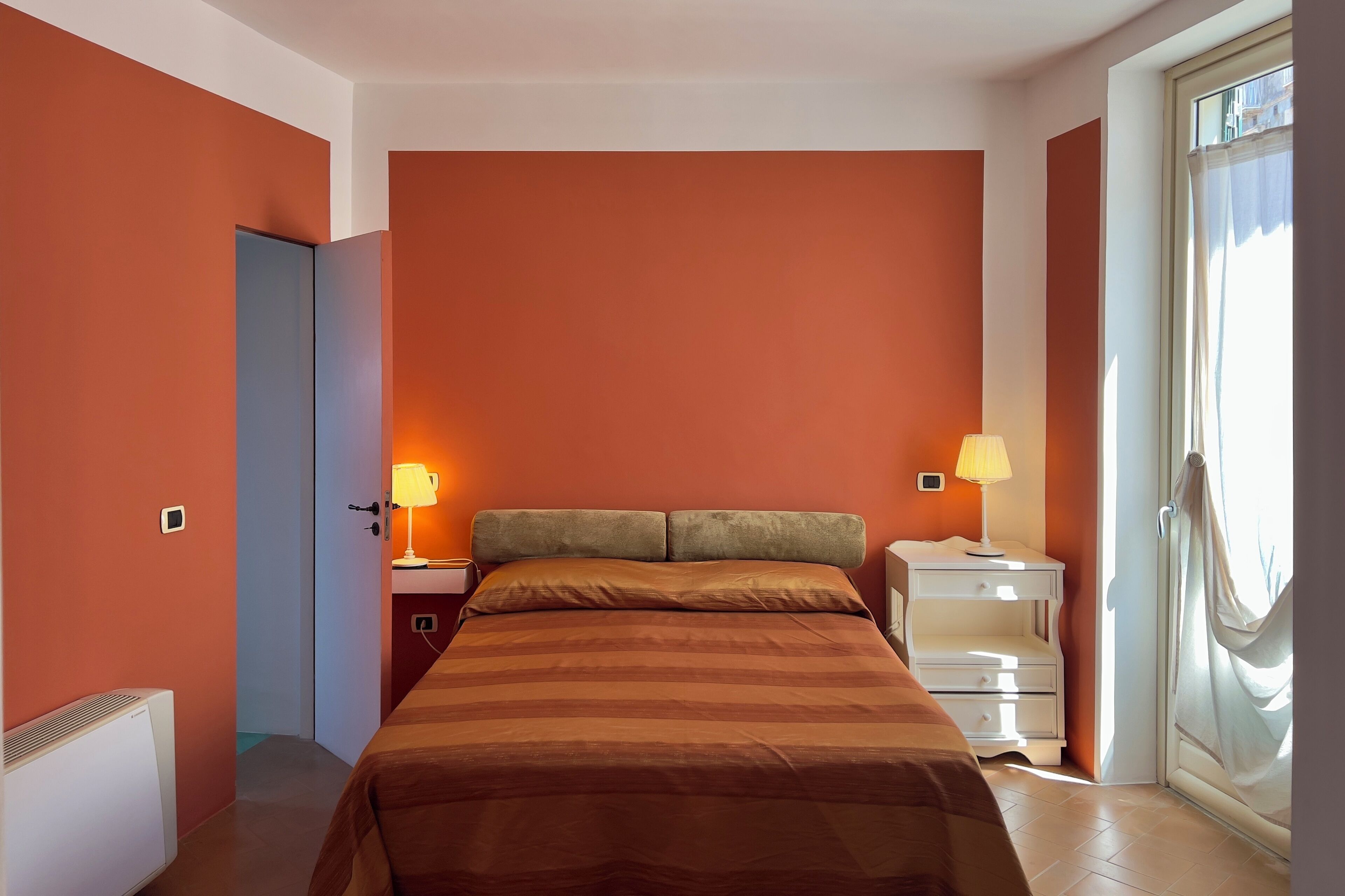 Une chambre à coucher comprenant un lit, deux tables de chevet avec des lampes, un radiateur et une porte donnant sur un balcon.
