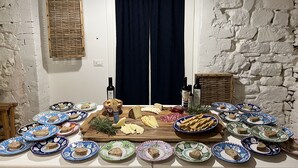 A room with a rustic stone wall, a wooden door with a dark curtain, and a table set with various cheeses, bread, and plates.
