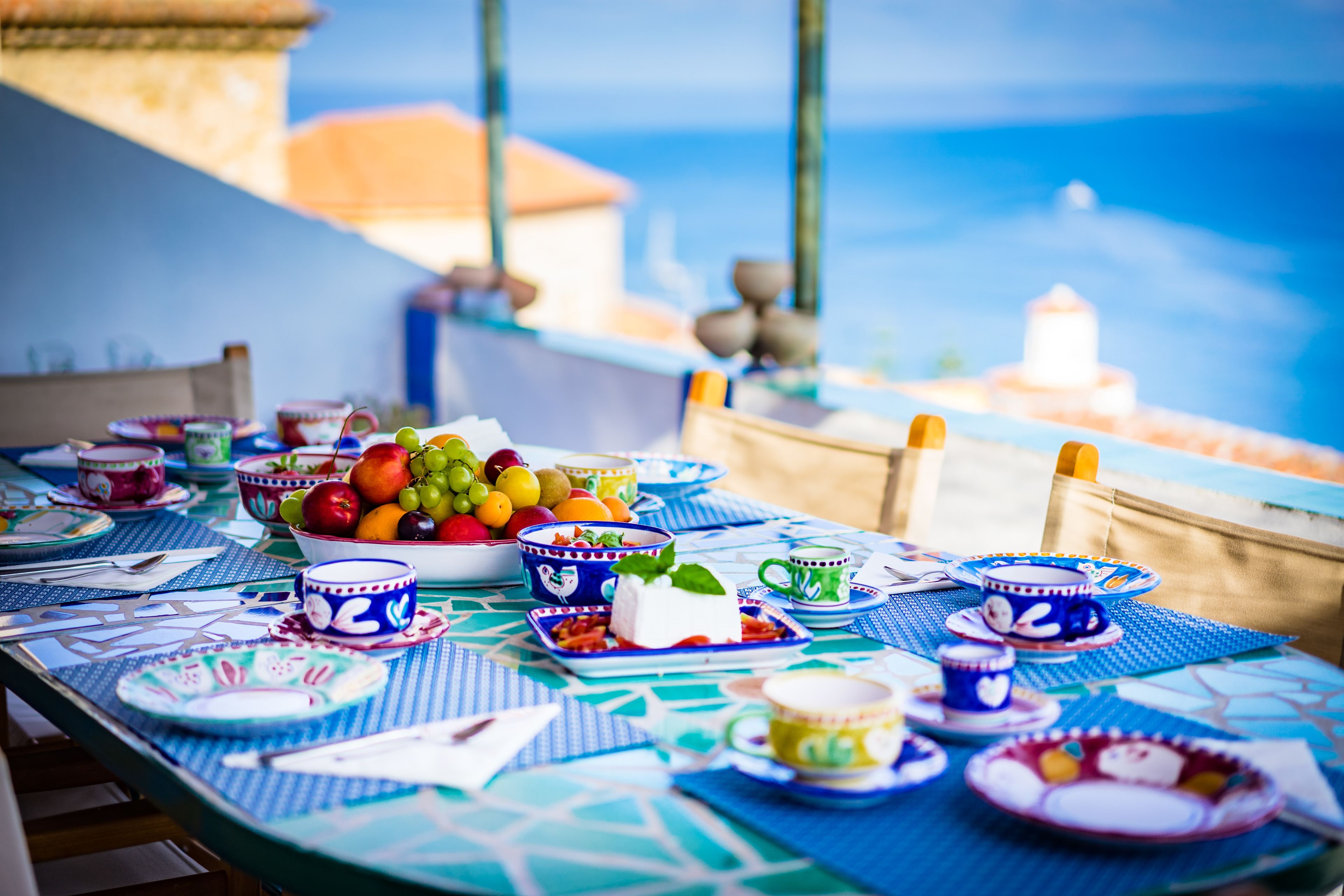 A table set with various dishes and drinks, overlooking a scenic view of the sea and buildings.