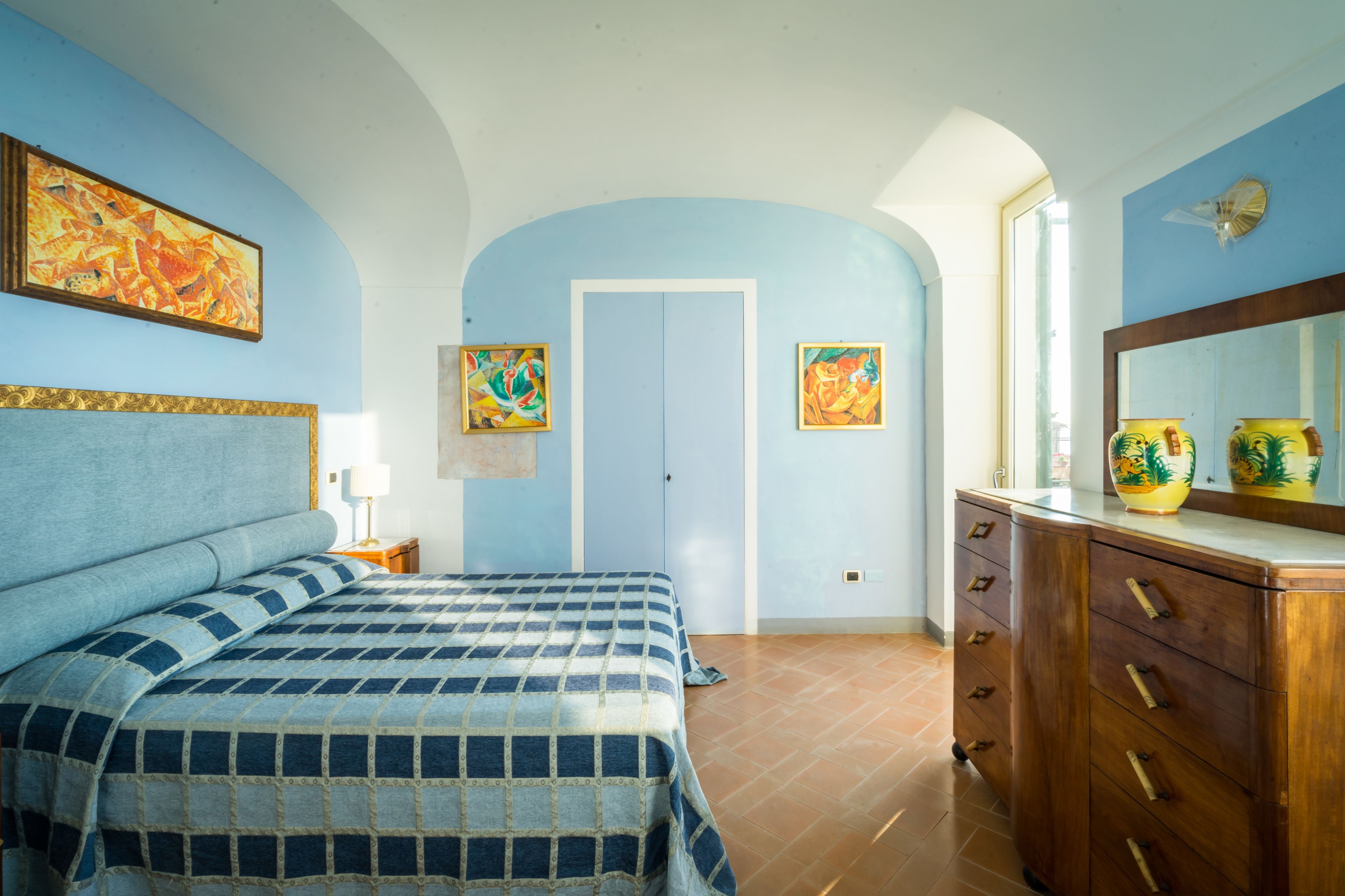 A bedroom with a bed, a dresser, and two paintings on the wall.