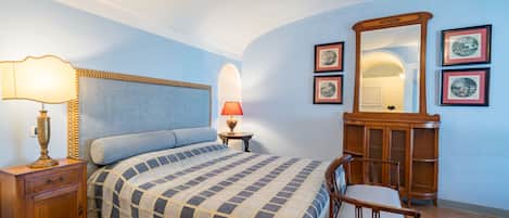 A bedroom with a bed, bedside table, lamp, dresser, chair, and framed pictures on the wall.