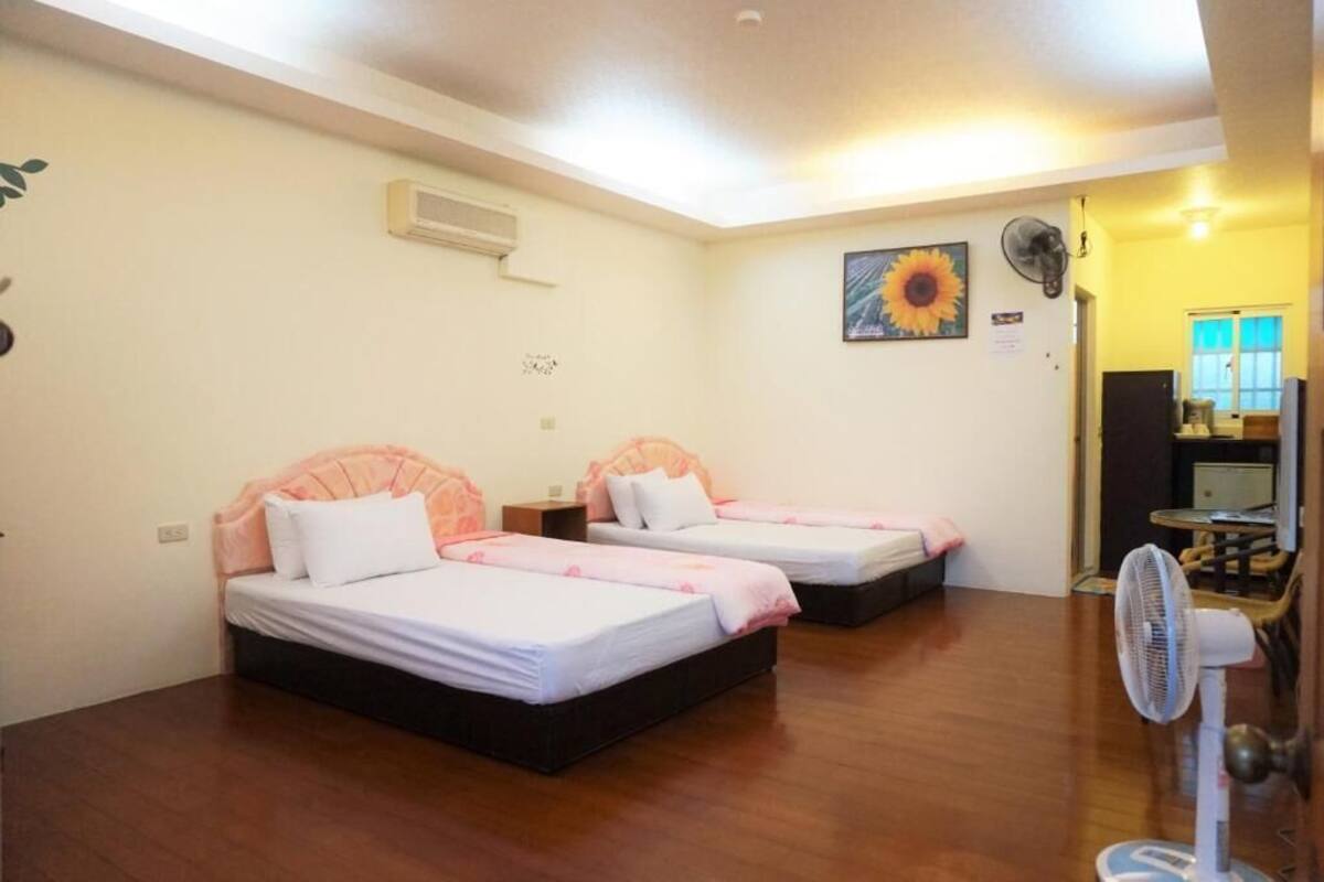 A hotel room with two beds, a ceiling fan, and a painting on the wall.