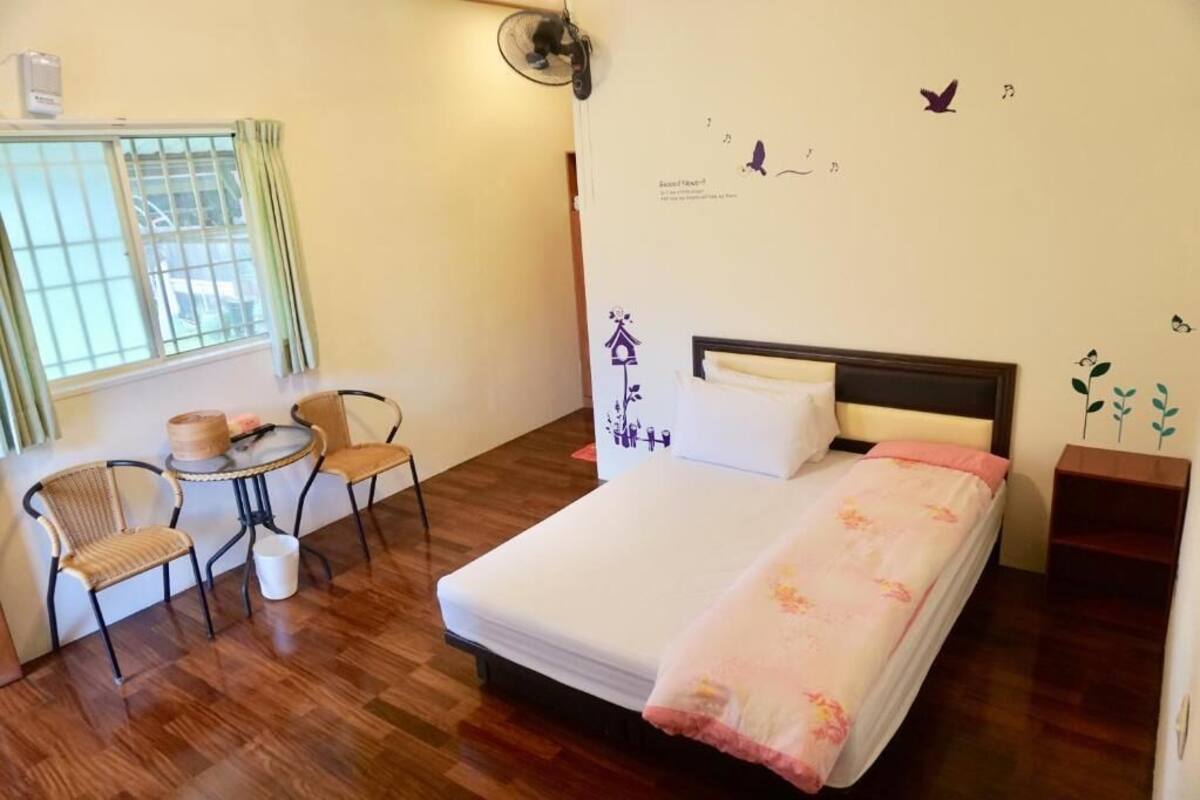 A bedroom with a bed, a chair, a small table, and a window with curtains.