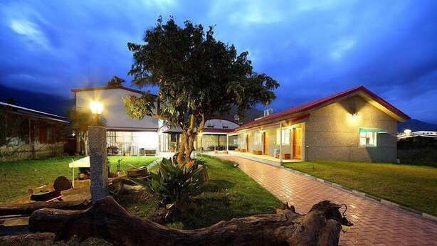 A two-story house with a paved pathway leading to the entrance, surrounded by a well-maintained lawn and a large tree. - Chin Shan B&B (Guanshan)