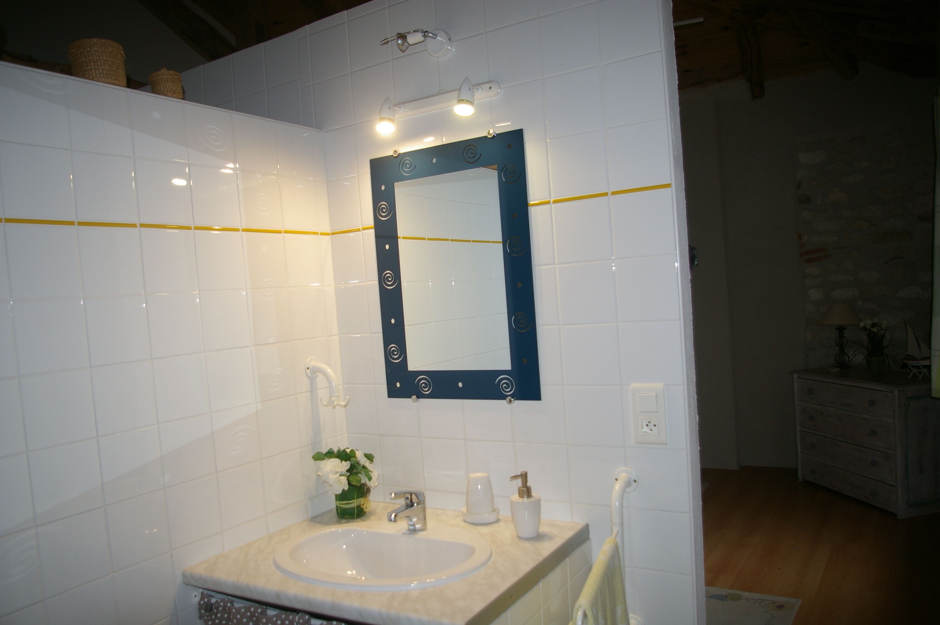 A bathroom with white tiled walls, a sink with a mirror, and a wooden floor.