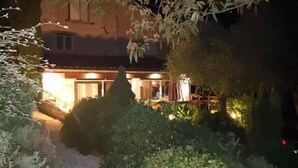 Een nachtzicht van een huis met een goed verlichte gevel, omgeven door weelderige beplanting en een grindpad dat naar de ingang leidt.