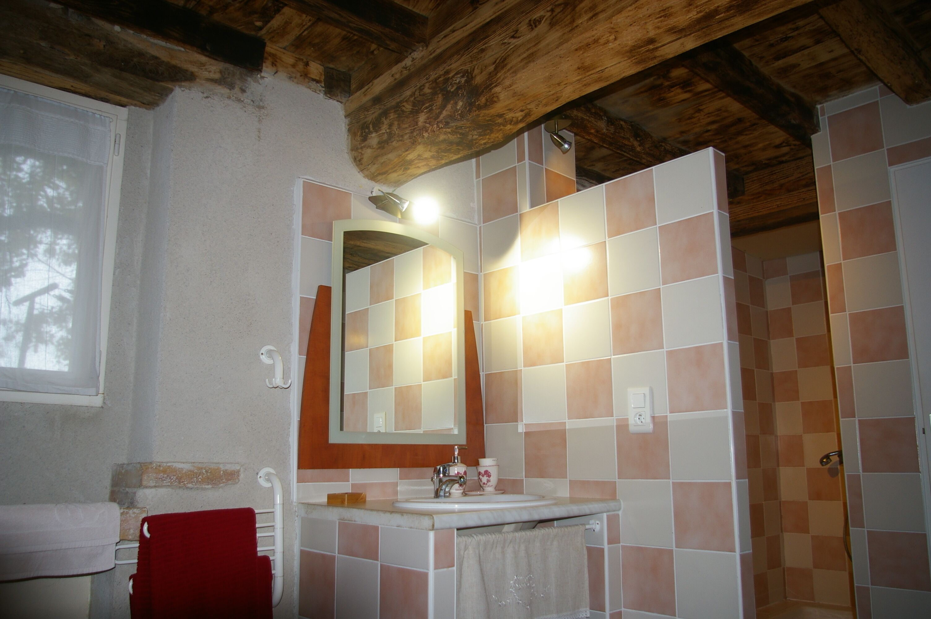 Ein Badezimmer mit Holzbalkendecke, einem weißen Waschbecken, einem Spiegel und Schachbrettfliesen.