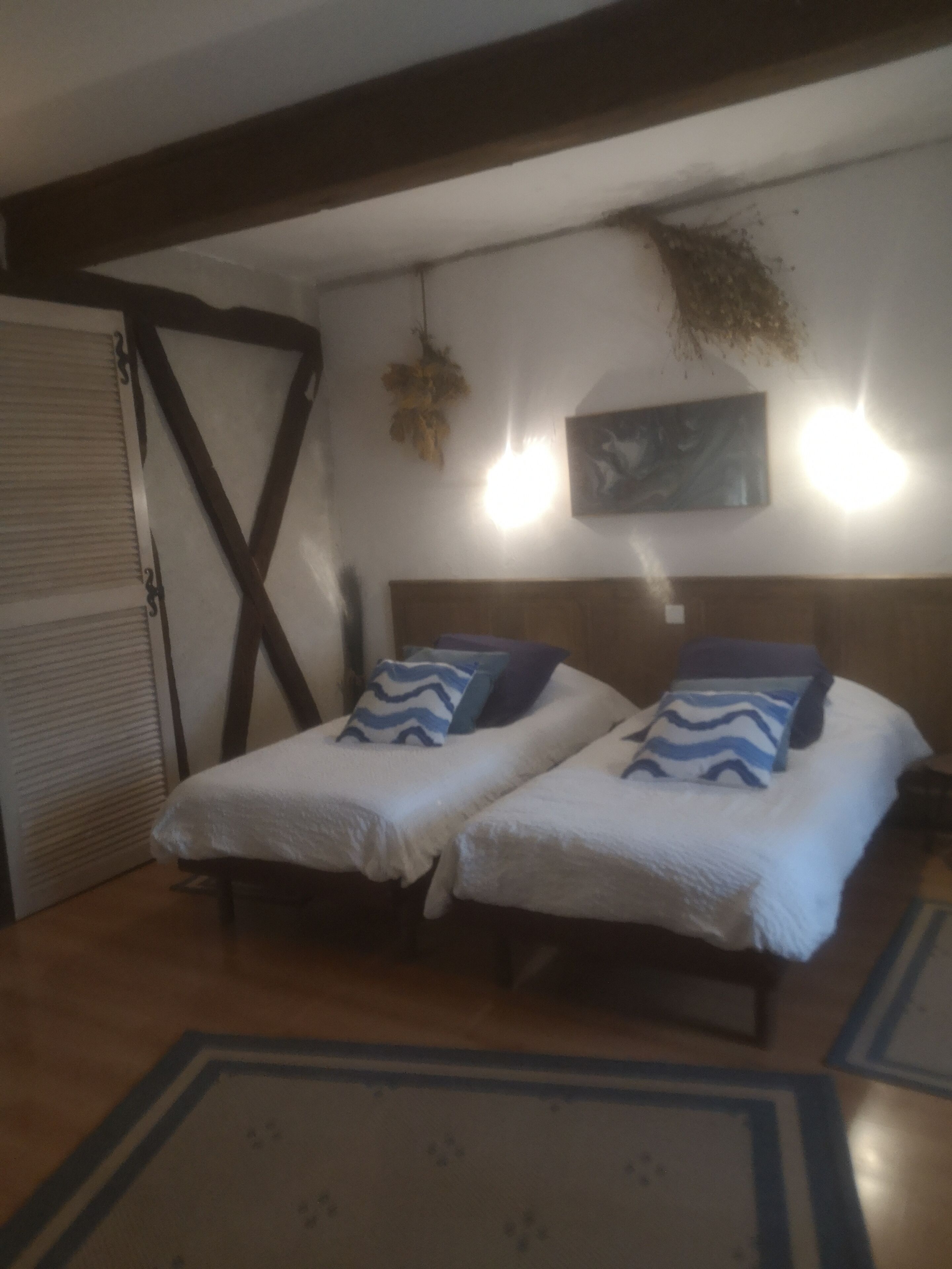 A room with two beds, a wooden ceiling, a wall-mounted light, and a door.