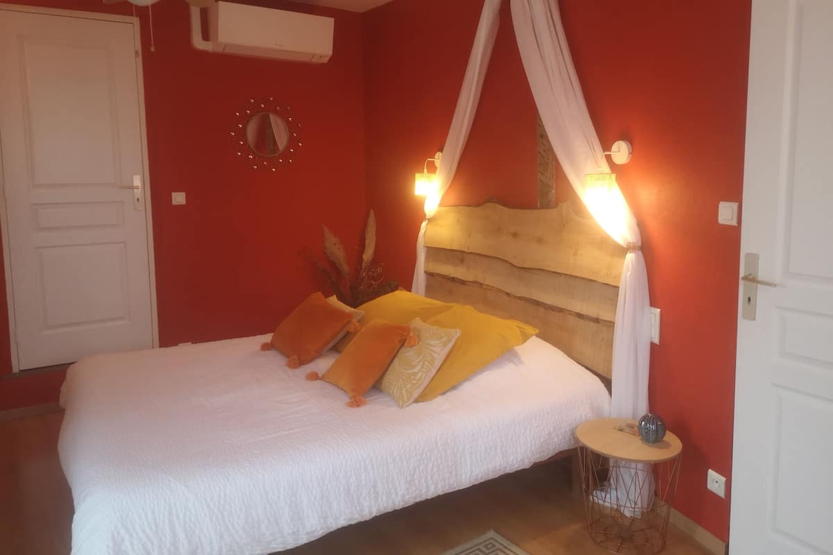 Een slaapkamer met een bed, witte gordijnen, een nachtkastje en een plafondventilator.