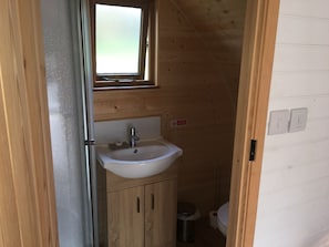 Un baño pequeño con revestimiento de madera, un lavamanos blanco, un espejo y una ventana.