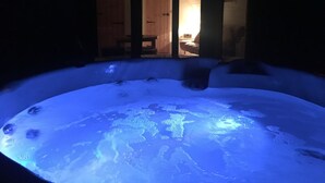 A hot tub in a dimly lit room with wooden doors leading to a brighter area. - Brynllwyd Glamping (Aberystwyth)