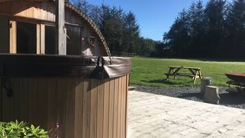 Un bain à remous en bois, avec une terrasse en bois et une table de pique-nique, situé dans un jardin.