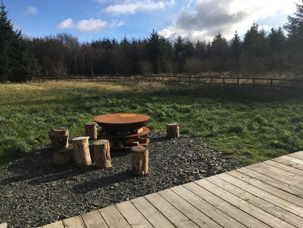 An outdoor wooden deck with a circular fire pit surrounded by logs.
