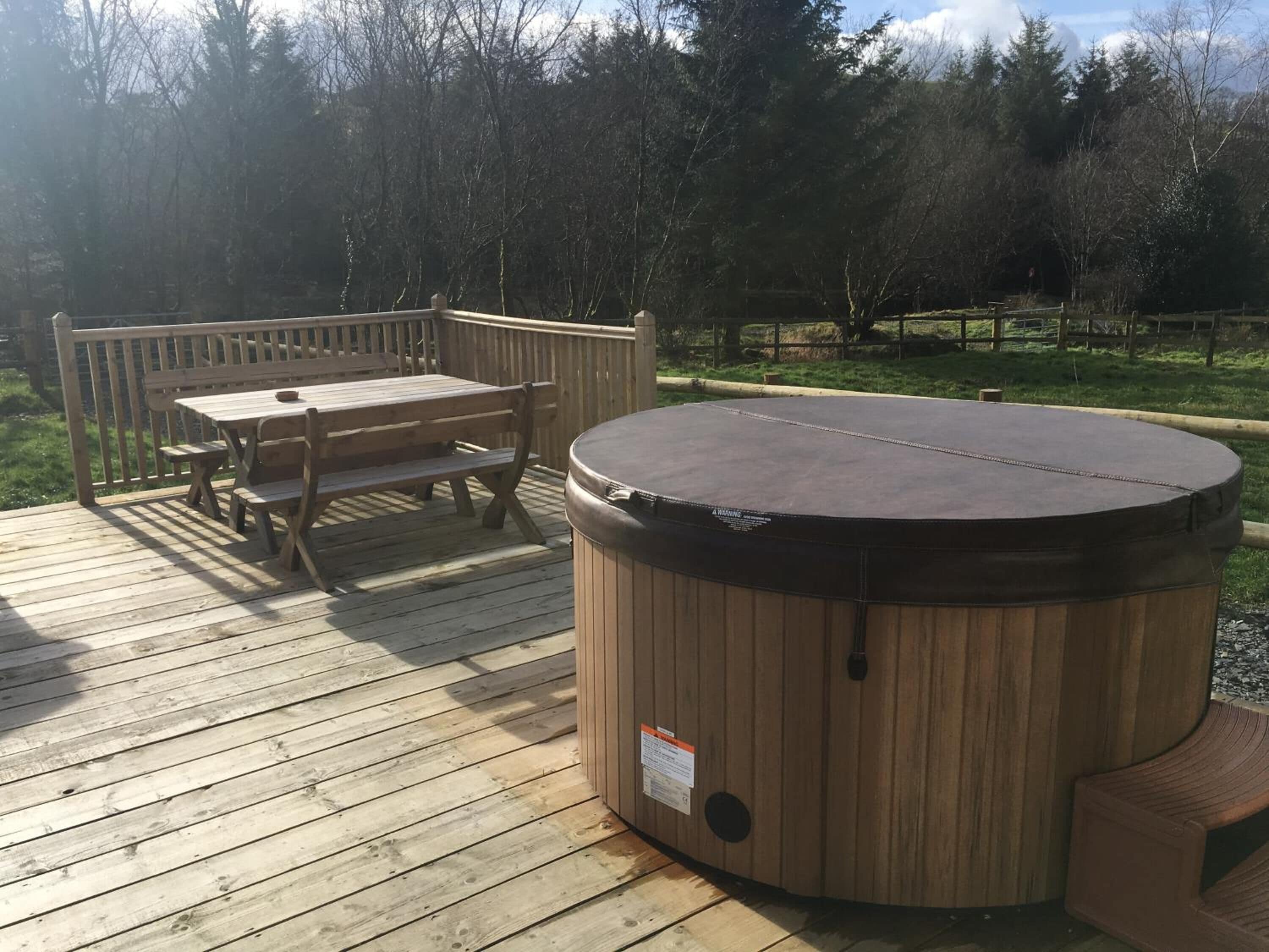 A wooden deck with a hot tub, a wooden table, and benches.