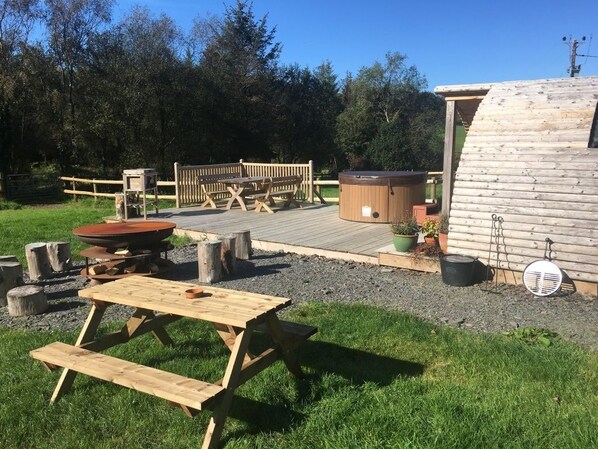 Una terraza de madera con mesas de picnic, un jacuzzi y una cabaña de madera.