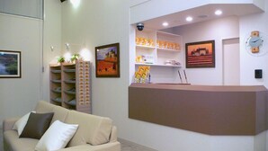 A reception area with a reception desk, a sofa, a shelving unit with plants, and framed pictures on the walls.