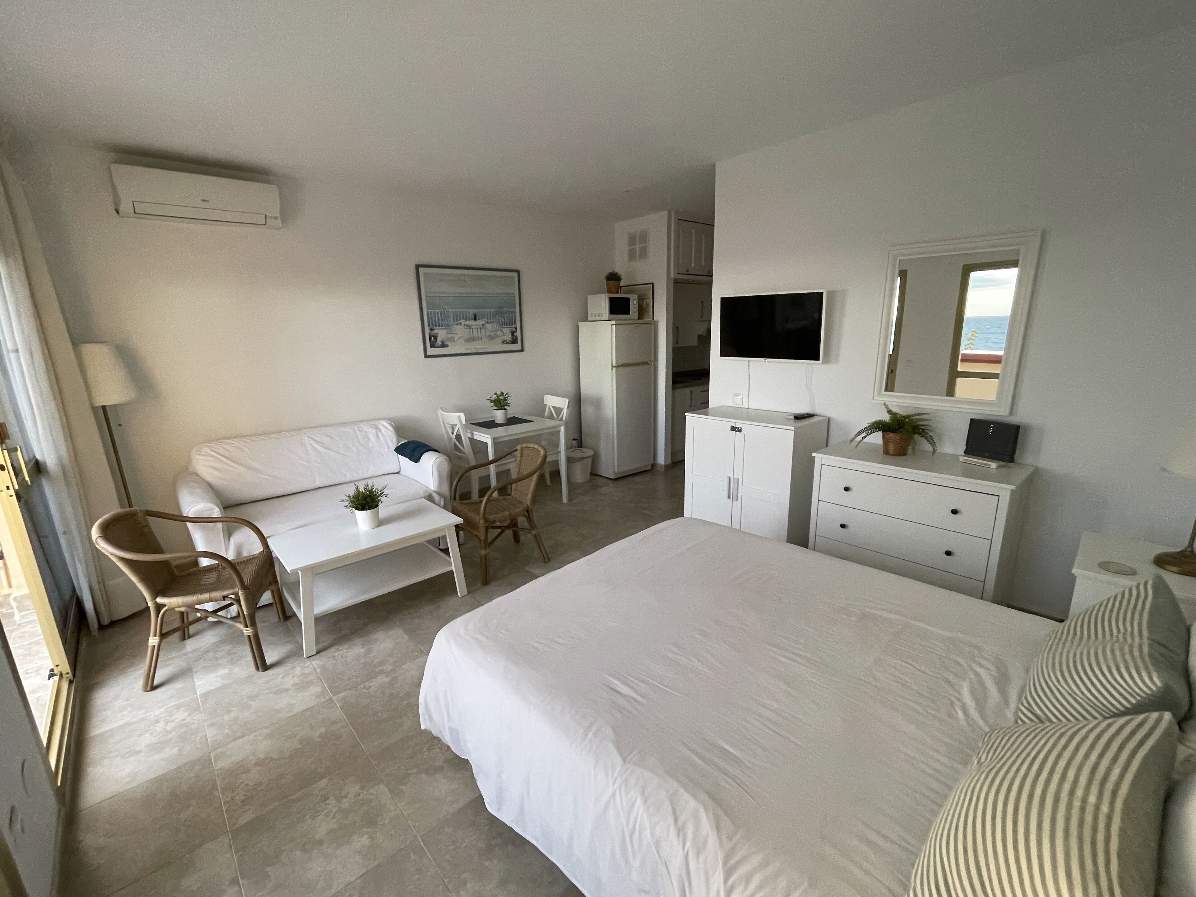 Quarto de hotel com cama, escrivaninha, cadeira, mesinha, cômoda, televisão e janela com vista.