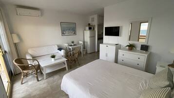 Quarto de hotel com cama, escrivaninha, cadeira, mesinha, cômoda, televisão e janela com vista.