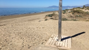 Una spiaggia sabbiosa con una struttura metallica, un pontile di legno e una vista aperta sull'oceano e sulle montagne in lontananza.