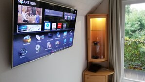 Ein an der Wand befestigter Flachbildfernseher zeigt verschiedene Apps und Sender, darunter eine Suchleiste und ein Bereich für Samsung Apps.