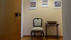 En hall med en dörr av trä, en stol och ett litet bord med en korg på. Tre inramade tavlor hänger på väggen.
