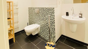 A bathroom with a toilet, a sink, a mirror, and a shower area. - BerlinLUX Apartments - City (Berlin)