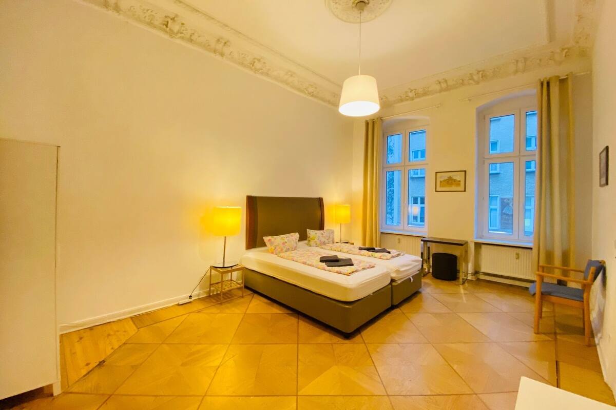 Ein Hotelzimmer mit einem großen Bett, zwei Nachttischlampen, einem Heizkörper und einem Fenster mit Vorhängen.