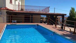 Ein Schwimmbecken mit Holzterrasse, ein Balkon mit roter Geländer und Blick aufs Meer.