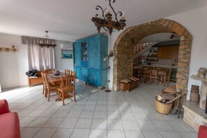 Un vaste espace de vie comprenant une table et des chaises, un buffet bleu, une arche en pierre et une cuisine visible à travers l’arche.
