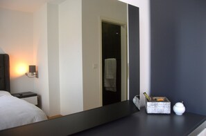 Une chambre d’hôtel comprenant un lit, une table de chevet, une commode, un miroir et une petite table sur laquelle se trouvent une boîte et un objet blanc.