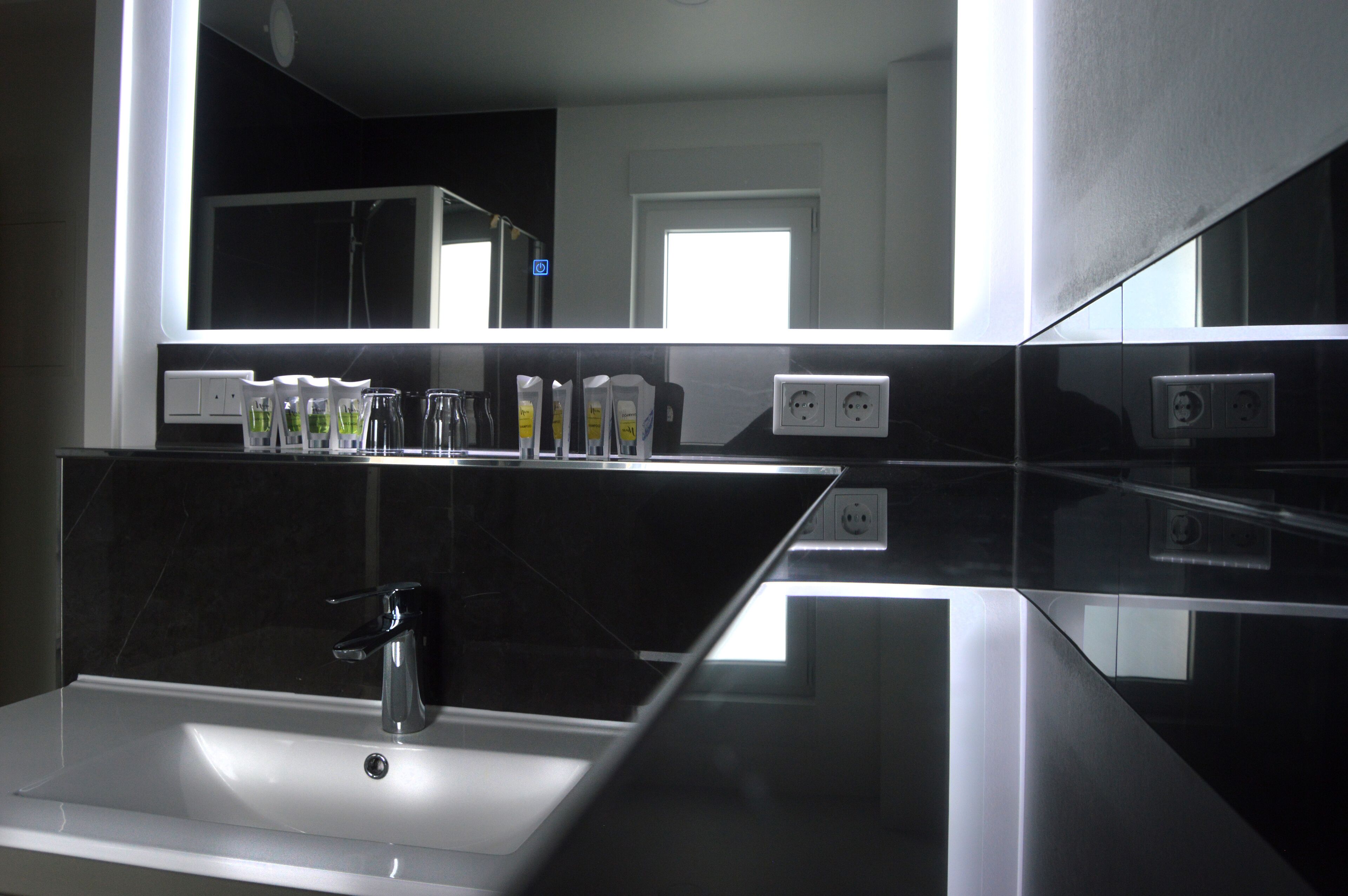 A modern bathroom with a large mirror, a sink, and a window providing natural light.