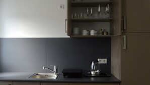 A modern kitchen with a sink, a kettle, and a shelf with glasses and cups.