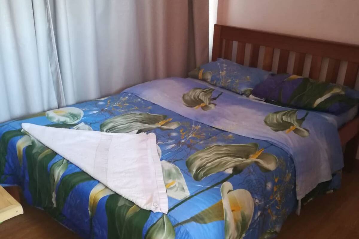 A double bed with a floral bedspread, a wooden headboard, and a white towel on the bed.