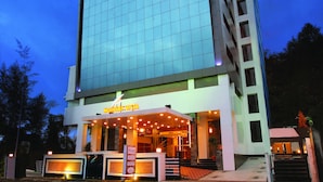 A modern hotel with a large glass facade, a prominent entrance with outdoor lighting, and a sign reading "Holiday Vista". - Holiday Vista (Peermade)