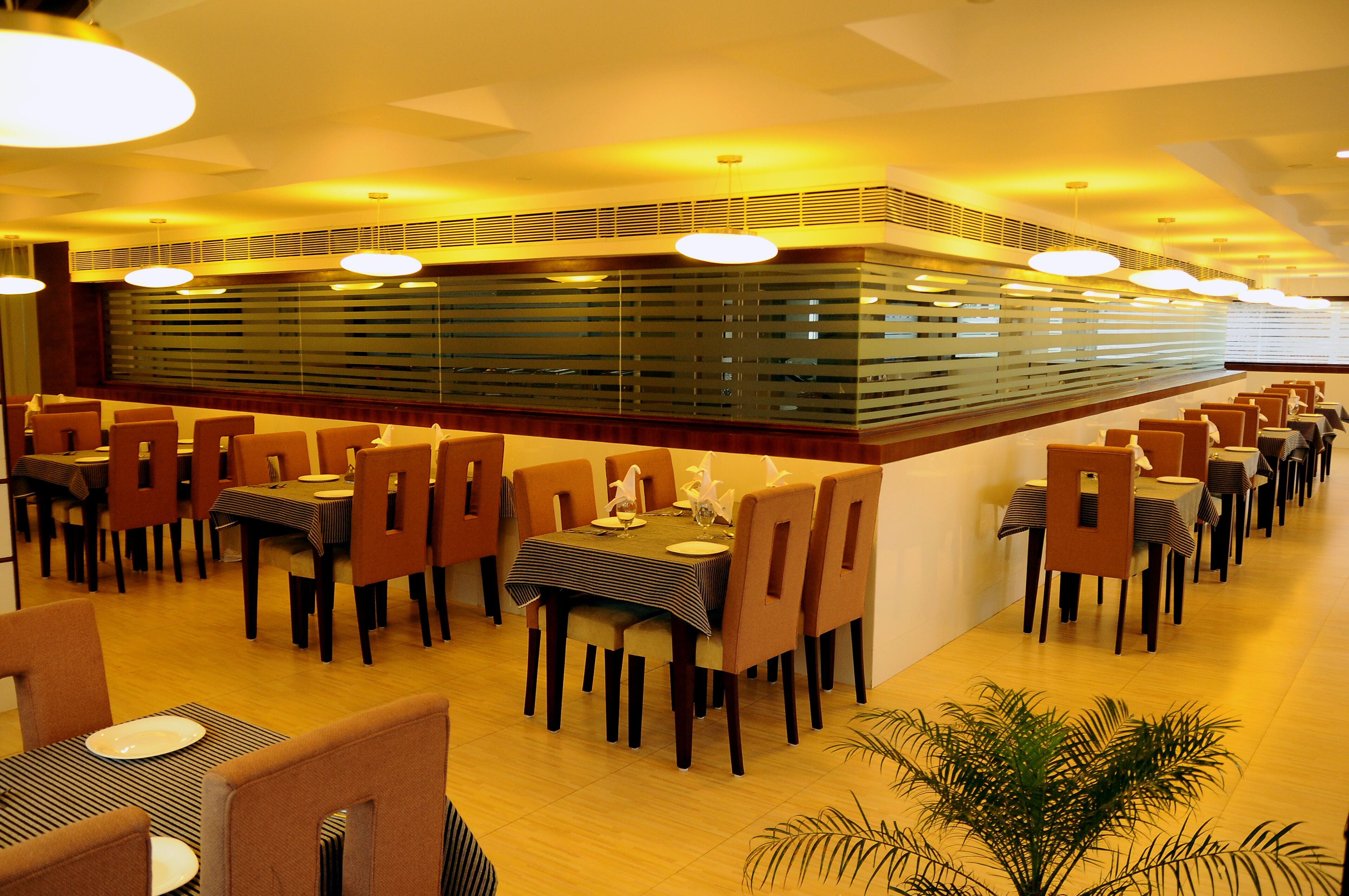 Een restaurant met meerdere tafels en stoelen, een decoratieve centrale muur en verlichting aan het plafond.