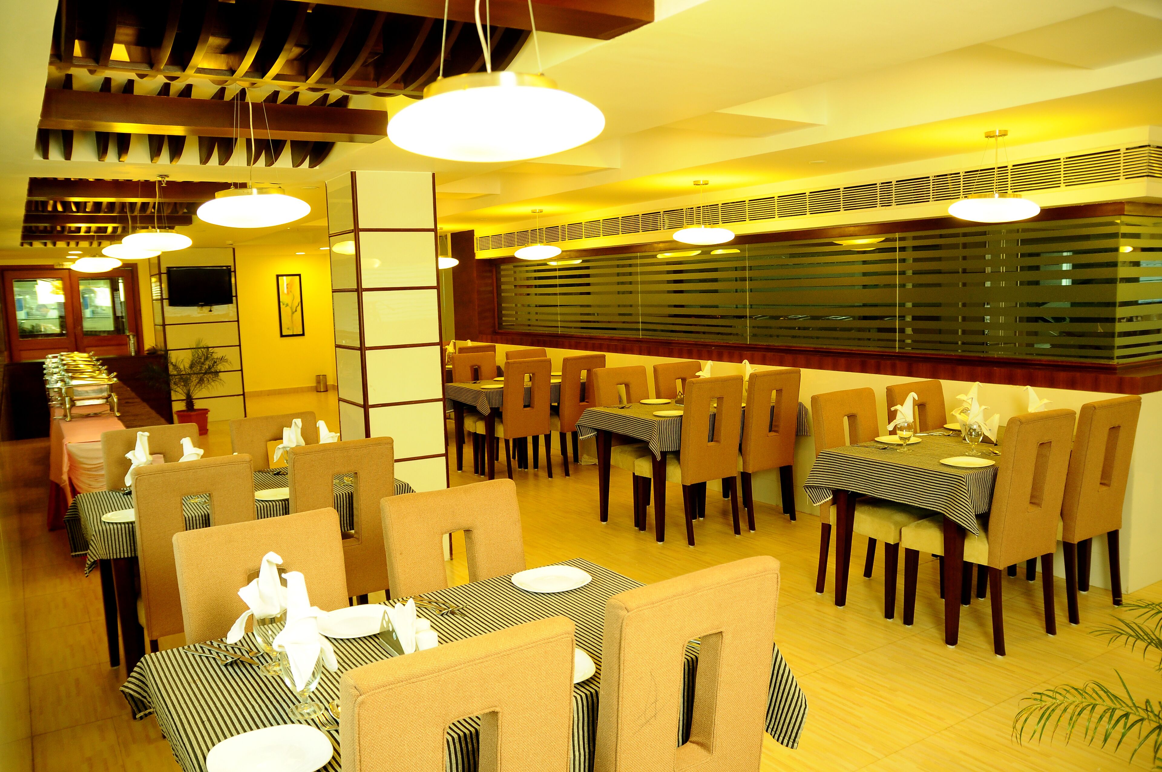 Un ristorante con diversi tavoli e sedie, una televisione montata a parete e un soffitto con travi a vista e luci a sospensione.