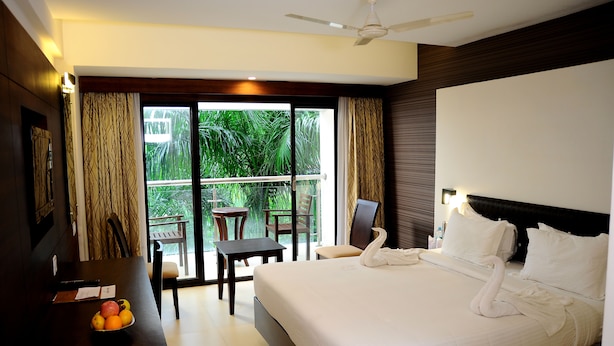 A hotel room with a bed, a dining table with fruit, a balcony with chairs, and a view of greenery. - Holiday Vista (Peermade)