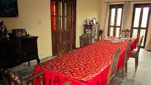 A dining room with a long table covered in a red tablecloth, wooden chairs, a cabinet, and a door with stained glass panels. - Hotel Mountain Ridge (Badharamal)