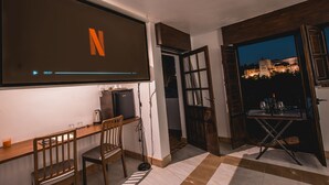 Ein Zimmer mit einem großen Bildschirm, der das Netflix-Logo zeigt, einem kleinen Tisch mit Gläsern und einer Flasche sowie Blick auf eine Burg bei Nacht.