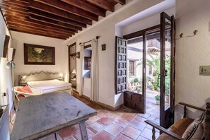 Una stanza con un letto, un tavolo e una porta aperta che dà su un balcone con piante.