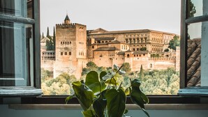 Ein Blumentopf auf einem kleinen Tisch neben einem Fenster mit Blick auf ein historisches Gebäude.