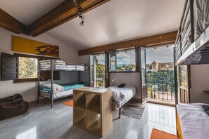 Una camera da letto moderna e open space con un letto a castello, un piccolo tavolino in legno e vista sulla città attraverso ampie finestre.