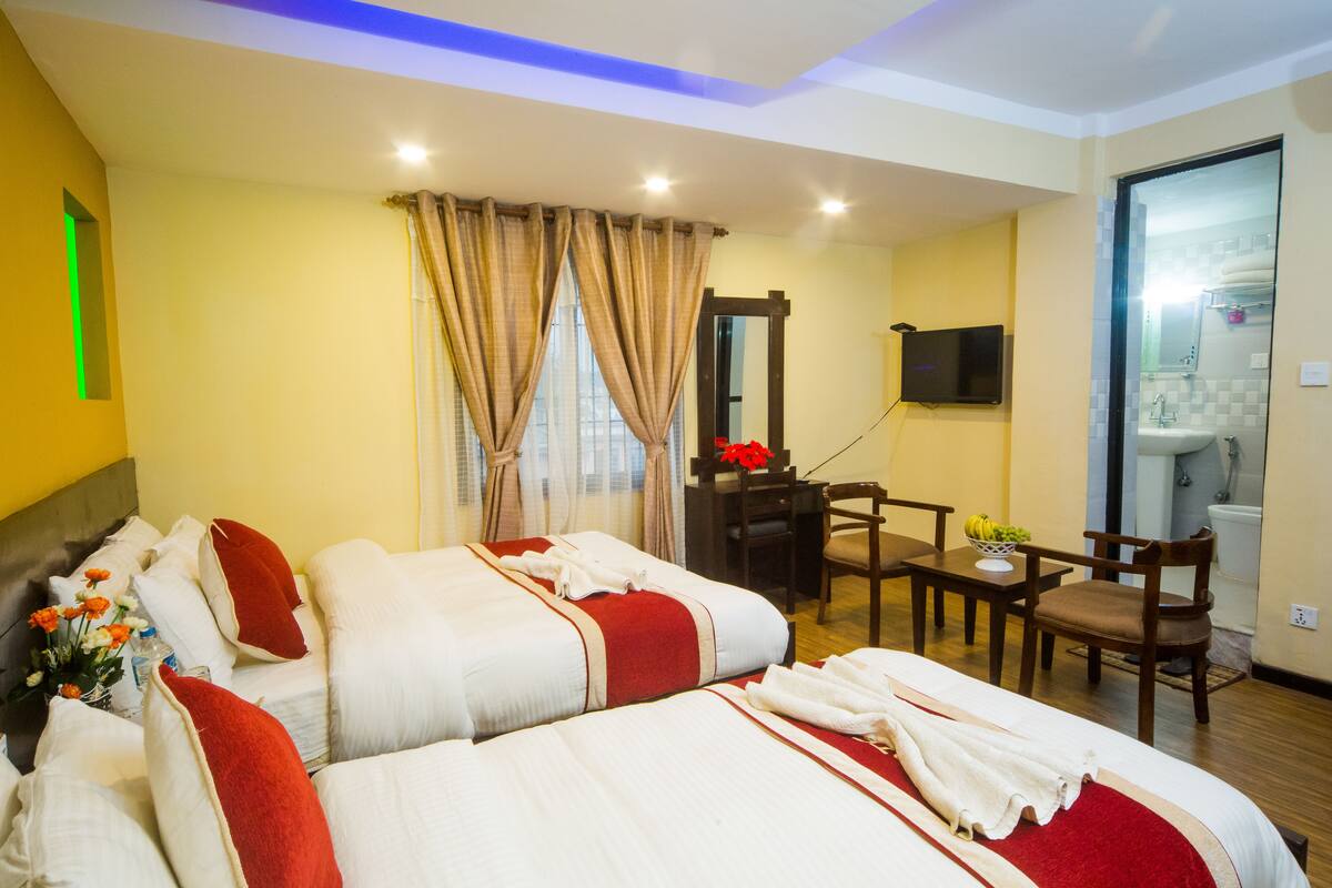 A hotel room with two beds, a desk, a chair, a TV, and a bathroom.