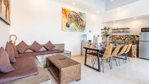 A modern living room with a sofa, ottoman, and dining area with chairs. - AV Villa Coco (Seminyak)