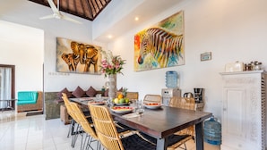 A dining area with a long wooden table, wicker chairs, and a white cabinet. - AV Villa Coco (Seminyak)